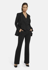 Zwart op maat gemaakt pak met een getailleerde blazer met een pieklapel, een button-up vest en slim-fit broek. Het materiaal lijkt glad met een gestructureerd ontwerp.