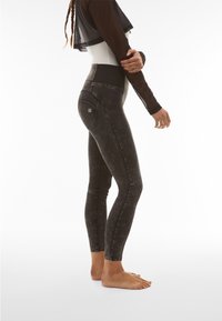 Leggings neri a vita alta con finitura testurizzata, caratterizzati da una vestibilità slim e tasche posteriori, mostrati di lato su piedi nudi.