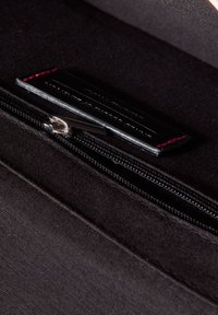 Černá látková taška s uzávěrem na zip, texturovaným vnitřkem a malou koženou visačkou s vyvýšeným textem. Jemný červený prošívání.