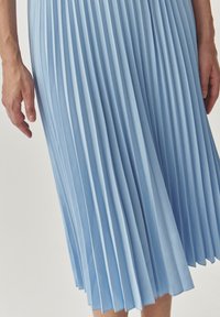 Fustă plisată de culoare albastru deschis, confecționată dintr-un material fin, având pliseuri înguste și uniforme și o siluetă fluidă. Prim-plan asupra texturii și detaliilor țesăturii.