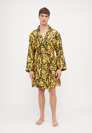 Robe giallo e nero a fantasia floreale, scollatura a V bassa, vita con cintura e maniche lunghe. Presenta due tasche frontali.