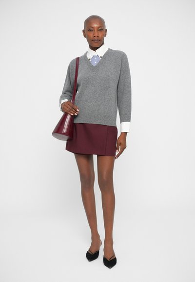 Grauer Strickpullover mit V-Ausschnitt, weißes Hemd mit blauen Streifen, bordeauxroter Minirock und burgunderfarbene Handtasche, kombiniert mit schwarzen High Heels.