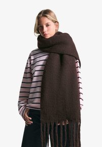 Sciarpa di lana marrone con una texture morbida e bordi frangiati, avvolta attorno al collo, abbinata a un top a strisce rosa e blu navy.
