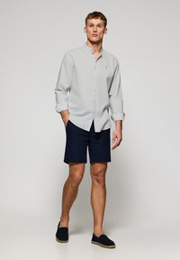 Ljusblå långärmad skjorta med knappar, mörknavy shorts och espadrillos. Skjortan har en bandkrage; tyget har en mjuk textur.