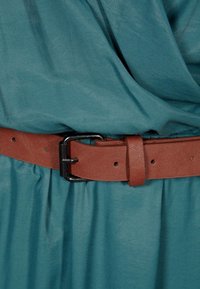 Teal fabric dress with pleats, cinched at the waist by a brown leather belt featuring a black metal buckle. Soft texture and smooth finish.