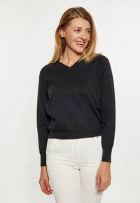 Czarny sweter z dekoltem w serek, wykonany z miękkiego materiału, z długimi rękawami, w połączeniu z białymi spodniami. Sweter ma dopasowany krój oraz prążkowane mankiety.
