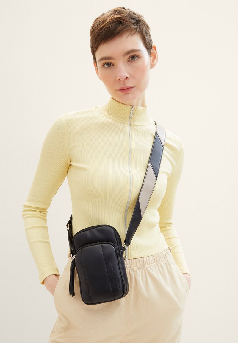 Borsa a tracolla nera con due scomparti con zip, texture liscia e una tracolla removibile con accenti marrone chiaro e grigio scuro.