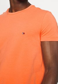 T-shirt arancione in cotone a maniche corte con colletto rotondo e piccolo logo ricamato sul petto. Tessuto liscio con leggera elasticità.