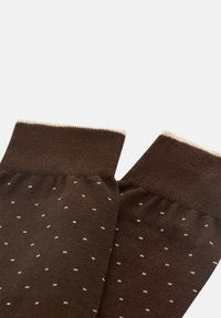 Rjave nogavice z fino teksturo, ki imajo majhne bele pike in bež obrobo. Oblikovanje je preprosto, poudarja vzorec in kontrast barv.