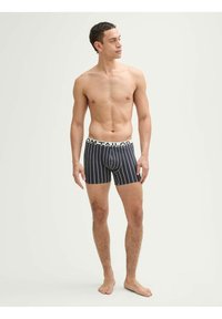 Fekete-fehér csíkos boxernadrág, márkázott rugalmas derékkal, bemutatva egy modell által, semleges háttér előtt.