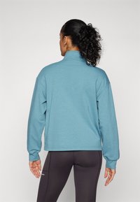 Hellblauer, übergroßer Pullover mit langen Ärmeln und hohem Kragen, ausgestattet mit einer glatten Textur und gerippten Bündchen.