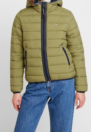 Olivenfarvet pufferjakke med lynlås foran, hætte og marineblå detaljer. Har vandret quiltet design og sidelommer med lynlås. Denimjeans synlige.