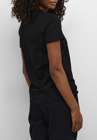 T-shirt en coton noir avec des manches courtes et un col rond classique, vu de dos. Texture douce et coupe ajustée.