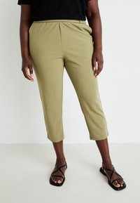 Olivgrön korta byxor med en slät yta, elastisk midja och sidofickor, kombinerade med svarta sandaler med remmar.
