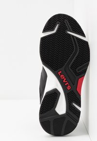 Černá pryžová podrážka tenisky s texturovaným vzorem rybí kosti. Obsahuje logo Levi's v červených a bílých akcentů na převážně černém designu.