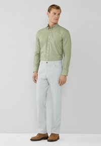 Hellgrünes Hemd mit Knöpfen, hellblaue Hose und braune Wildlederschuhe. Das Hemd hat einen Kragen und Knöpfe, die Hose verfügt über Taschen.