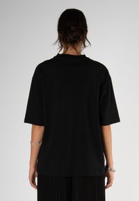 Camiseta de algodón negra con mangas cortas y un corte relajado. Diseño liso, cuello redondo y color sólido sin patrones ni logotipos visibles.