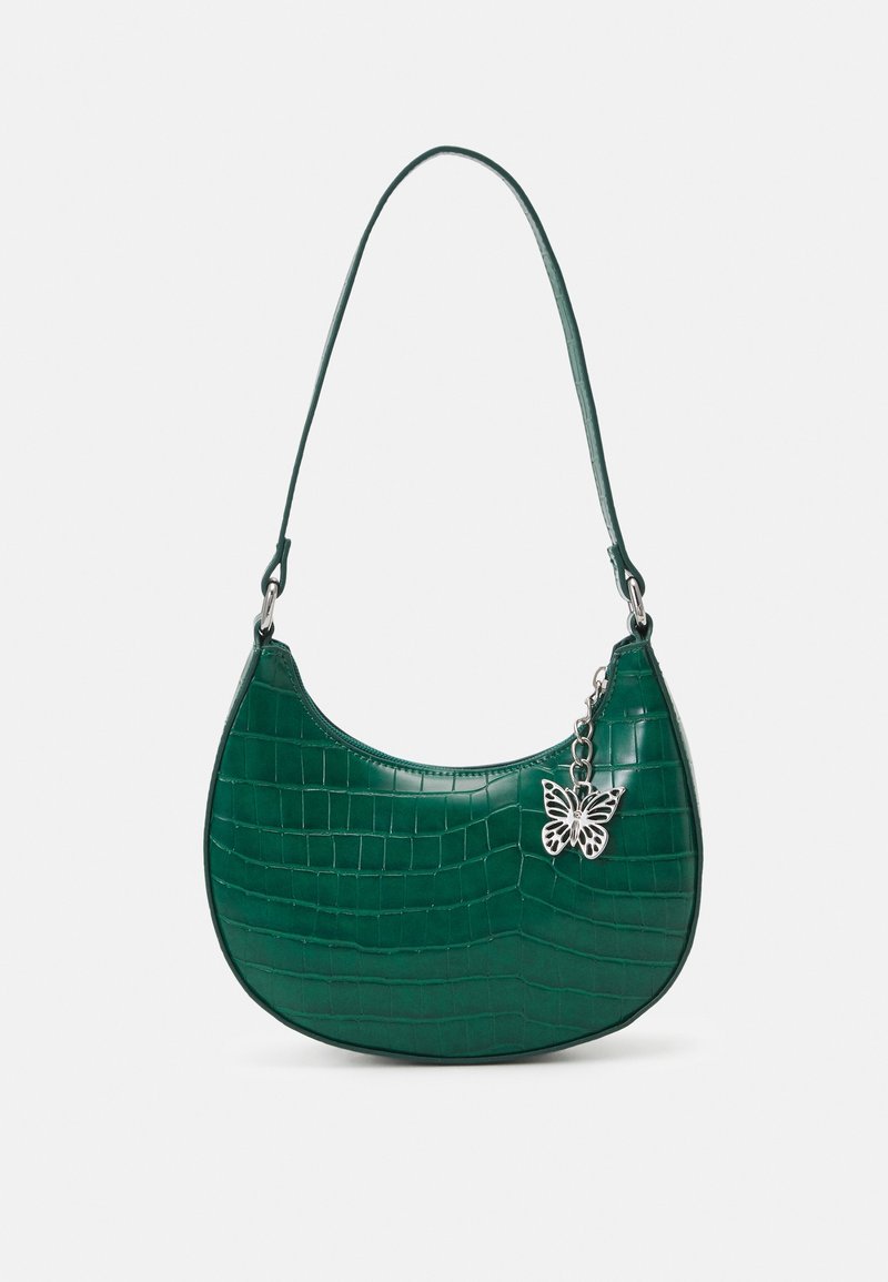 Sac à épaule vert à motif crocodile, forme courbée, breloque papillon argentée et bandoulière unique sur fond blanc.