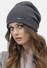 Grå strikket beanie med slouchy design, der har et lille metallic-logo fortil. Blød tekstur og let løs pasform.