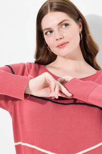 Różowy sweter dzianinowy z szerokim dekoltem, prążkowanymi rękawami oraz poziomymi paskami w kolorze kremowym i granatowym. Miękka tekstura i luźny krój.