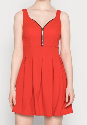 Robe sans manches rouge avec un décolleté en V, dotée d'un détail de fermeture éclair noire et d'une jupe plissée, fabriquée dans un tissu lisse.