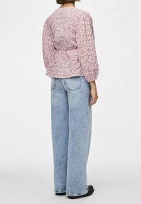 Blusa rosa con motivo floreale e maniche a sbuffo, abbinata a jeans a vita alta azzurri a gamba larga e scarpe nere, vista dalla schiena.