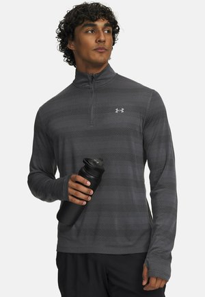 Grauer Sportpullover mit Reißverschluss, strukturiertem Muster, langen Ärmeln und Daumenlöchern, kombiniert mit einer schwarzen Wasserflasche in der Hand.