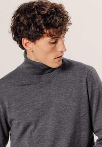 Grijze, gebreide coltrui met een gestructureerde afwerking en een relaxte pasvorm. De stof lijkt zacht en warm, geschikt voor koeler weer.