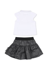 Un haut sans manches blanc avec un col associé à une jupe noire présentant une texture froncée et brillante, ainsi qu'une taille élastique.