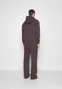 Tmavě šedá bavlněná mikina s kapucí a odpovídající kalhoty s volným střihom, žebrovanými manžetami a bočními švy. Hladká textura, minimalistický design.