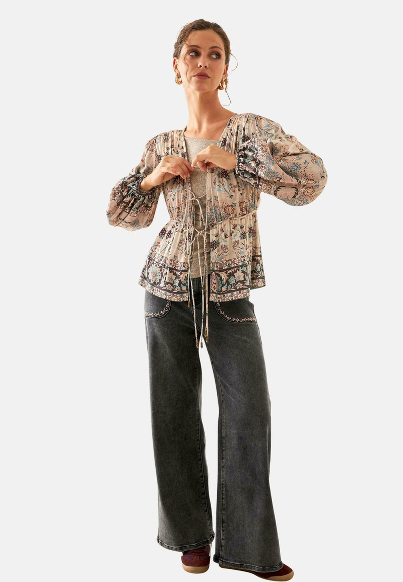 Blusa ligera con estampado floral, mangas abullonadas y detalle de cordón, combinada con pantalones grises de pierna ancha y acentos bordados.