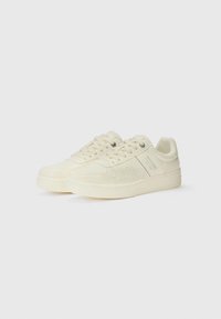 Light beige sneakers with perforated detailing and laces, featuring a subtle logo on the side, set against a plain white background.