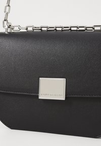 Schwarze Lederhandtasche mit glatter Textur, ausgestattet mit einem silbernen quadratischen Verschluss und einem Kettenriemen mit rechteckigen Gliedern.