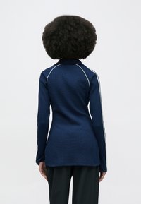 Navy blue long-sleeve top with a textured fabric, featuring white piping along the shoulders and sleeves. Classic collar design.