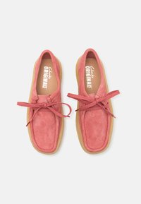Pink suede shoes with a rounded toe, lace-up design, and exposed stitching. Rubber sole with a natural finish. Brand name visible inside.