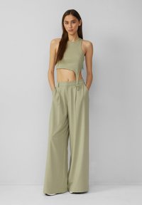 Šviesiai alyvuogių žalios spalvos juostuota trumpa palaidinė su išpjova, derinama su plačiomis, aukštai juosmeniu kelnėmis tos pačios spalvos, turinčiomis šonines kišenes.