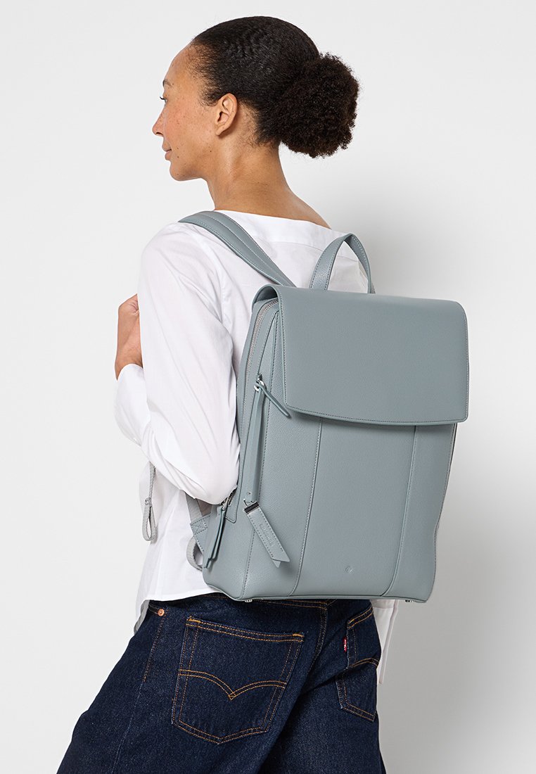 Grau Leder Rucksack mit strukturiertem Design, Klappenverschluss, verstellbaren Trägern und dezenten genähten Akzenten. Glatte Textur, minimalistischer Stil.