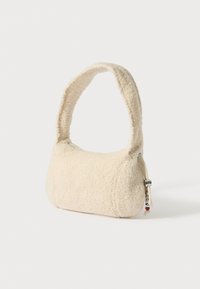 Béžová kabelka z umělého beránka s zaobleným tvarem, silným uchem a kovovým zipem. Kompaktní tvar vhodný pro každodenní použití.