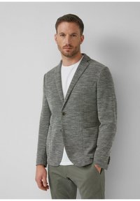 Grijze textuur blazer met een enkele knoop aan de voorkant, geknipte revers en twee voorzakken, gecombineerd met een witte t-shirt en olijfgroene broek.