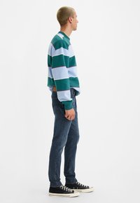 Long-sleeve striped sweatshirt in green, blue, and white; paired with dark blue jeans and black sneakers. Features a crew neck design.