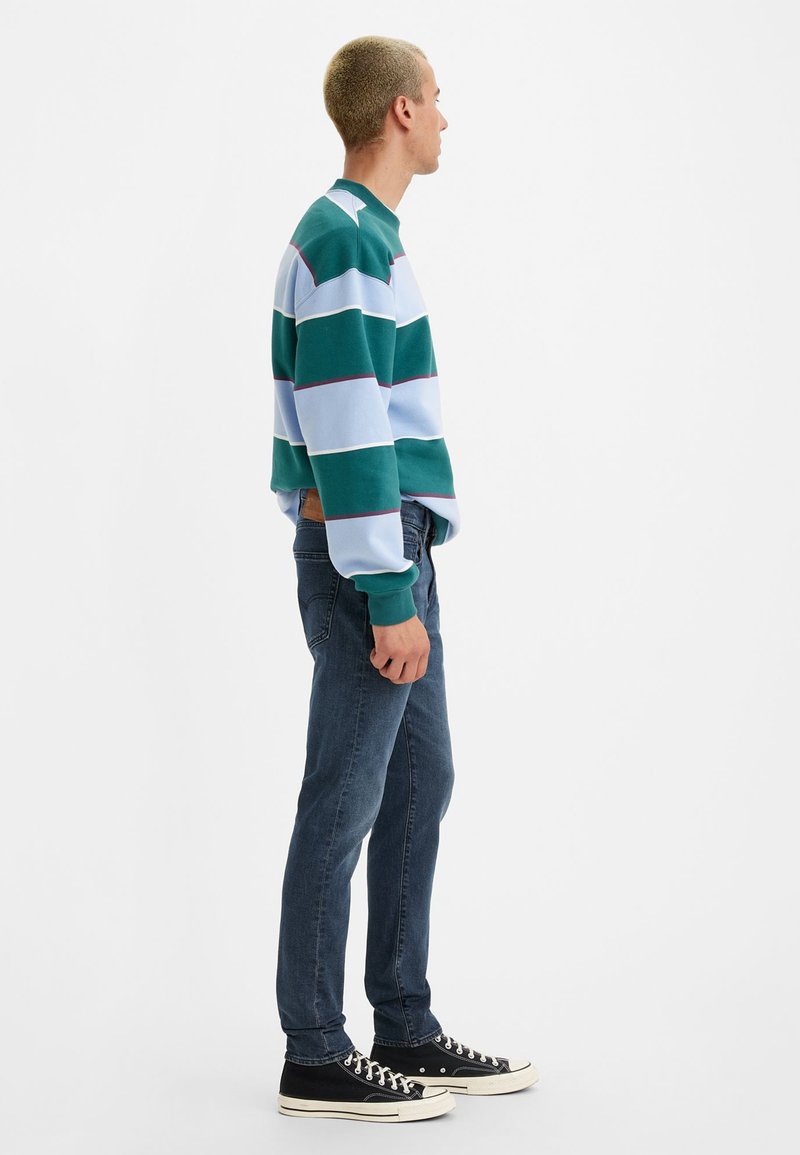 Sweat-shirt à rayures longues en vert, bleu et blanc ; associé à un jean bleu foncé et des baskets noires. Présente un design à col rond.