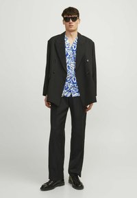 Blazer negro de doble botonadura sobre una camisa de rayas azul y blanca, combinado con pantalones y zapatos negros. Las gafas de sol completan el atuendo.