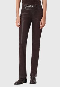 Pantaloni in pelle marrone con vestibilità slim, vita alta, tasche frontali e cuciture a contrasto. Texture liscia con finitura lucida.