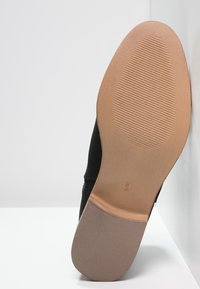 Czarna cholewka buta wykonana z gładkiego, elastycznego materiału, z jasnobrązową gumową podeszwą z teksturowanym wzorem, który zapewnia przyczepność.