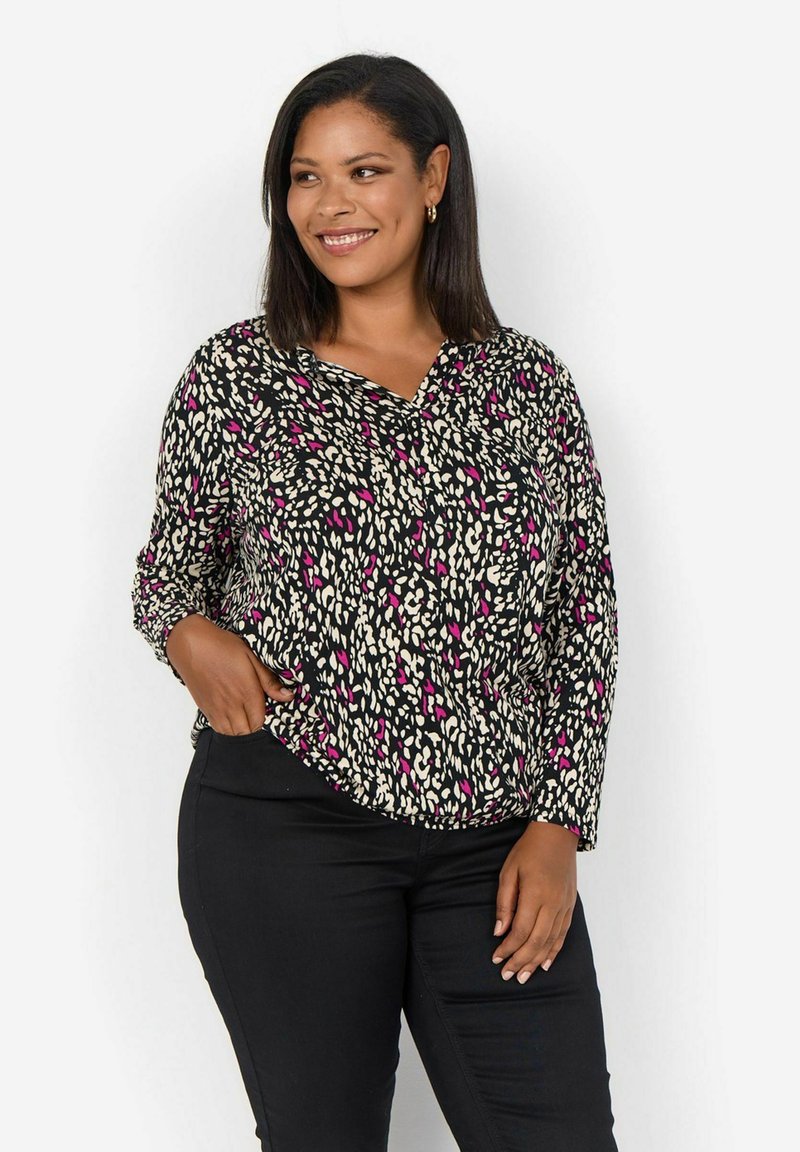 Blouse noire à manches longues avec un motif léopard mettant en avant des accents roses et crème. Encolure en V et coupe légèrement ample. Associée à un pantalon noir.