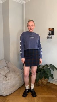 Kort marineblå genser med hvite motiver, kombinert med et rutete miniskjørt i marineblått og brunt, brukt med hvite sokker og svarte sko.