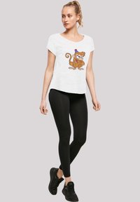 Hvitt t-skjorte med korte ermer som har et tegneserieape-design, kombinert med svarte leggings og svarte joggesko. Enkelt, avslappet antrekk.