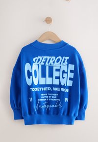 Blå sweatshirt med rund halsudskæring og lange ærmer. Har fed hvid tekst, der inkluderer "DETROIT COLLEGE" og "Unstoppable." Blødt stof.