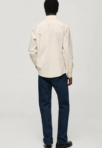 Light-colored, long-sleeve button-up shirt with a striped pattern, paired with dark blue jeans, viewed from the back. Black shoes visible.