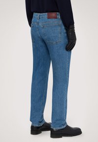 Niebieskie dżinsy o prostym kroju, z brązową skórzaną łatą na pasku i czarnymi skórzanymi rękawiczkami. Dolny brzeg jest lekko przetarty.